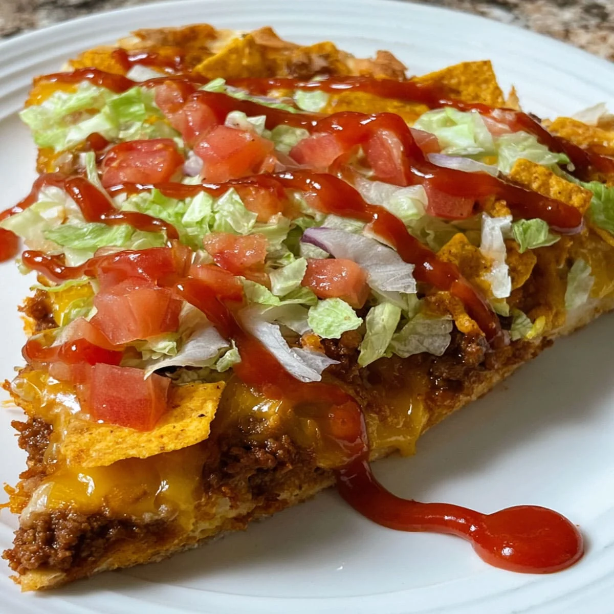 Best Homemade Taco Pizza for Family Dinner Ideas 79 Close-up of taco pizza slice topped with ground beef, cheese, lettuce, tomatoes, crushed Doritos, and a drizzle of taco sauce.