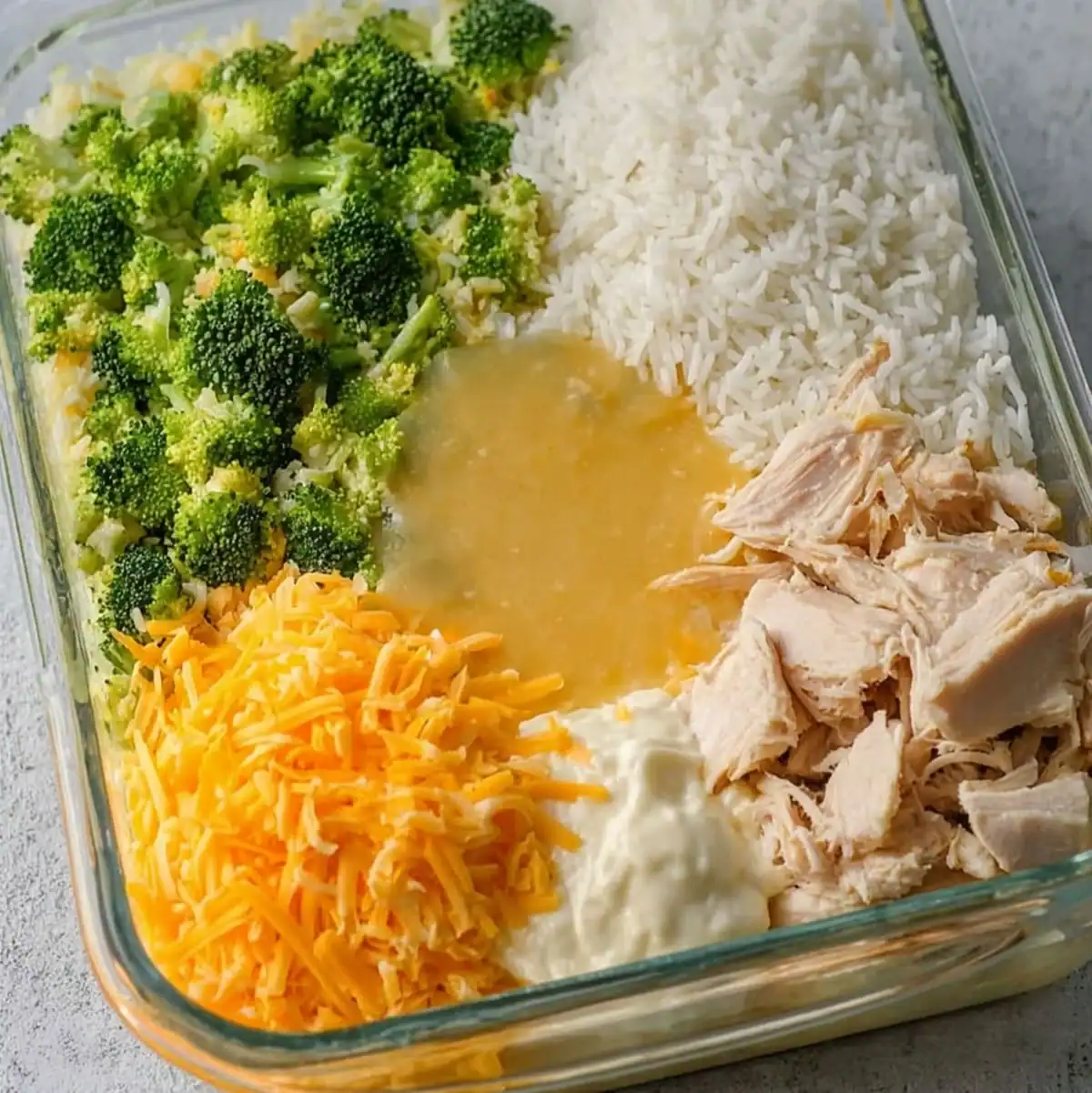 Best Cheesy Chicken Broccoli Rice Casserole 57 Fresh broccoli, shredded cheddar cheese, cooked rice, shredded chicken, cream of chicken soup, and mayonnaise layered in a glass baking dish for casserole.