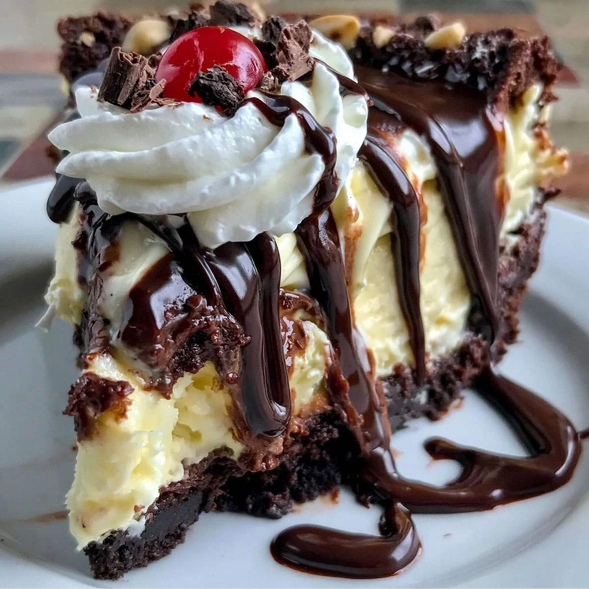 Ultimate Hot Fudge Sundae Brownie Cheesecake dessert with chocolate sauce, whipped cream, brownie layer, and maraschino cherry