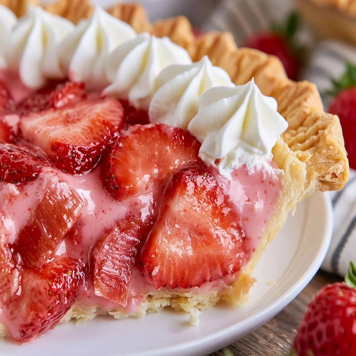 Strawberry Rhubarb Pie with close-up view of glossy strawberry slices, pink rhubarb chunks, whipped cream, and buttery crust