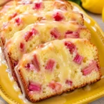 Lemon Rhubarb Bread sliced on a yellow plate with glossy lemon glaze, pink rhubarb pieces, and fresh lemons in the background.