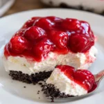 No Bake Cherry Cheesecake Dessert Recipe with creamy filling, glossy cherry topping, Oreo crust, and a spoonful bite on a white plate.